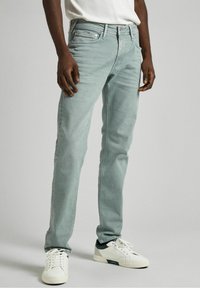 Jeans in denim verde chiaro con una vestibilità slim, design a cinque tasche e leggera scoloritura. Accompagnati da sneakers bianche con dettagli verdi.