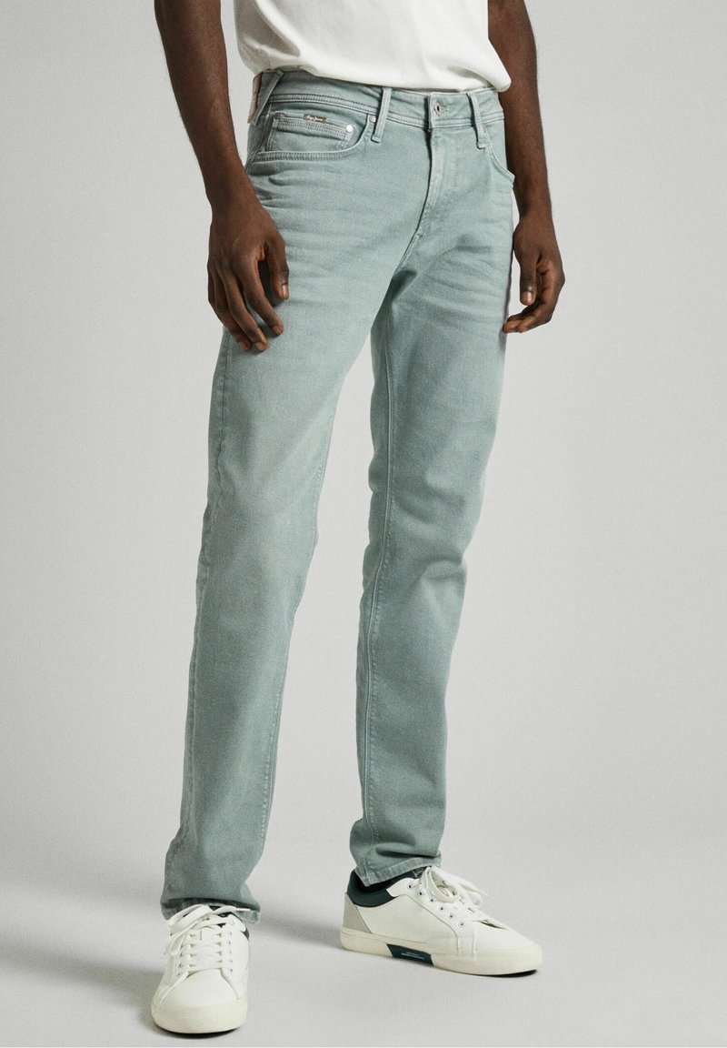 Jeans in denim verde chiaro con una vestibilità slim, design a cinque tasche e leggera scoloritura. Accompagnati da sneakers bianche con dettagli verdi.