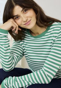 Young woman with long brown hair wearing a green and white striped sweater, resting her head on her hand and smiling gently.