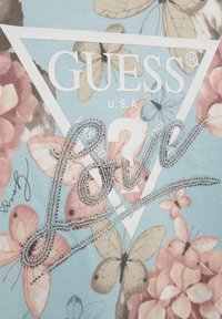 T-shirt azzurro chiaro con stampa floreale, un logo triangolare bianco e la parola "Love" in paillettes argento con un design in corsivo.