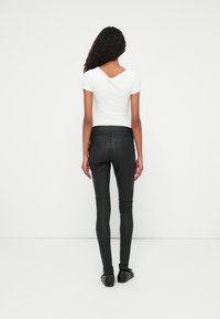 Fekete műbőr nadrág slim fit fazonnal, magas derékkal és sima felülettel. Fehér, rövid ujjú blúz kerek hátkivágással.