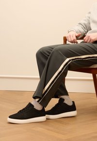 Sneaker nere con suola bianca, tomaia in pelle testurizzata e lacci tonali, abbinate a pantaloni tuta verde scuro con strisce bianche.