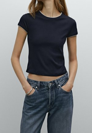 Marineblå croppet t-shirt med korte ærmer og en kontrasterende hvid halsudskæring, kombineret med højtaljede mørke denimjeans.