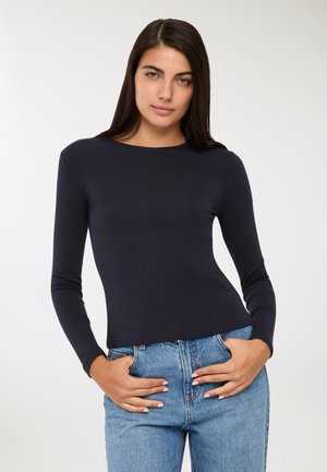 Maglietta a maniche lunghe blu navy in tessuto morbido con scollatura rotonda e design aderente, abbinata a jeans a vita alta di colore azzurro chiaro.