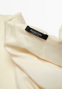 Beige stof med en glat tekstur, med et sort mærke med "Massimo Dutti" og "Made in Italy" i hvid tekst.