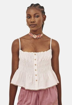 Top peplum de algodón blanco con tirantes finos, botones en el centro y textura fruncida. Acentuado con un borde de encaje en el dobladillo.