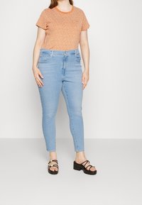 Orange kortärmad topp med vitt mönster, i kombination med ljusblå skinny jeans. Svarta blockklacksandaler fulländar outfiten.