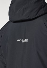 Čierna bunda Columbia Titanium s kapucňou, hladkým povrchom a výrazným bielym logom na chrbte. Minimalistický dizajn a odolný materiál.