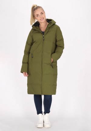 Piumino verde oliva con cappuccio, chiusura frontale con zip e tasche laterali. Presenta una texture trapuntata ed è lungo fino al ginocchio, abbinato a jeans blu e sneakers bianche.