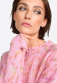 Pull en tricot rose avec une coupe décontractée, présentant un motif texturé et des touches de couleurs variées. Encolure ronde et poignets côtes.