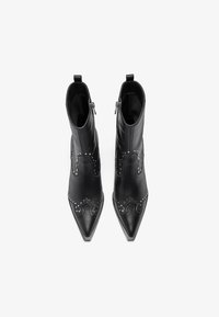 Botas de cuero negro hasta el tobillo con punta afilada, que presentan acentos bordados y tachuelas plateadas a lo largo de los lados. Cierre de cremallera en la parte posterior.