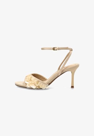 Sandalia de tacón alto para mujer en color beige con correa en el tobillo y lentejuelas redondas decorativas en la tira frontal.