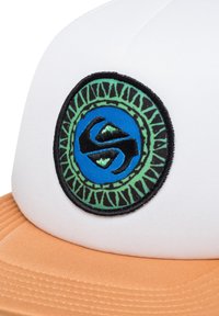 Witte pet met oranje rand, voorzien van een ronde geborduurde patch. De patch heeft blauwe en groene kleuren met een zwarte rand en ingewikkelde ontwerpelementen.