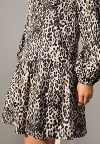 Vestito a stampa leopardata in beige e nero con gonna arricciata, maniche lunghe a sbuffo e texture morbida, caratterizzato da una vestibilità comoda e polsini elastici.