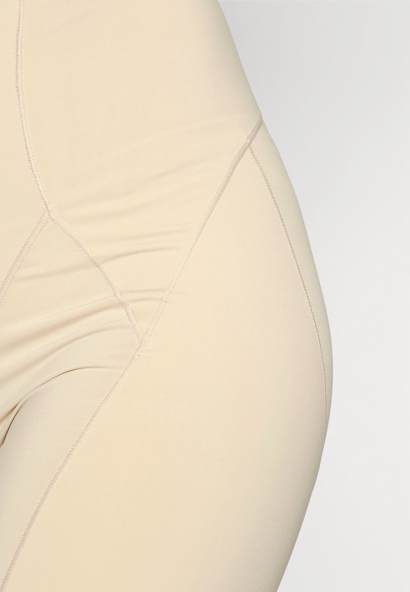 Leggings beige sin costuras con una textura suave, que presentan costuras curveadas y un diseño ajustado. Tejido ligero adecuado para superponer.