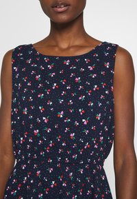 Granatowa sukienka w kwiatowy wzór w kolorach różowym, czerwonym i zielonym. Bez rękawów, o okrągłym dekolcie, z marszczoną talią i lekkim materiałem.