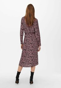 Abito a maniche lunghe di colore rosa con motivo a strisce zebrate nere, vita stretta e silhouette fluida. Abbinato a stivaletti neri alla caviglia.