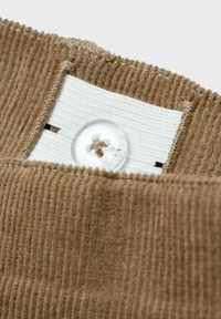 Tessuto in corduroy marrone con righe verticali, dotato di una fascia elastica bianca e un bottone trasparente con un piccolo accento marrone.