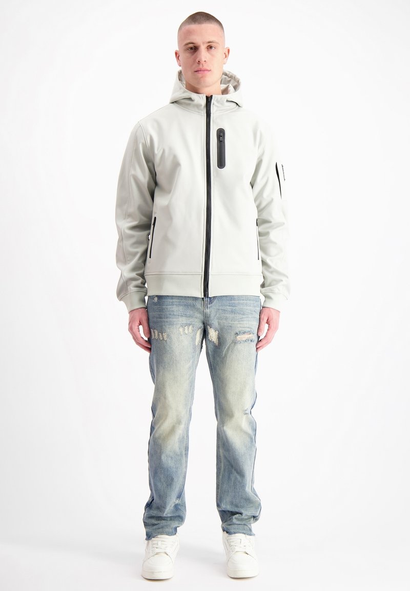 Lichtgrijze zip-up hoodie met zwarte rits en zakaccenten; gedragen met versleten blauwe spijkerbroek en witte sneakers.