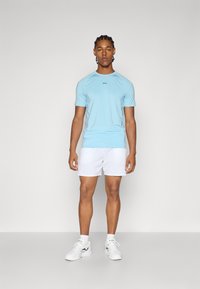Lyseblå kortærmet træningsshirt med sort logo, parret med hvide shorts og hvide træningssko. Simpelt design og glat tekstur.