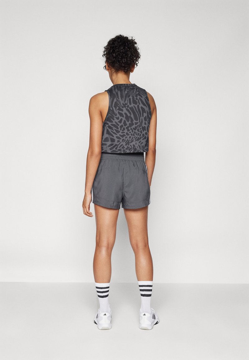 Tanktop in dunkelgrau mit Tiermotiv, kombiniert mit grauen Sportshorts. Das Modell trägt gestreifte weiße Socken und weiße Sneaker.