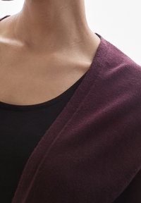 Burgundowy szalowy kołnierz, miękka tekstura, luźny krój na czarnej bluzce, podkreślający czysty dekolt i minimalne detale szwów.