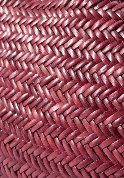 Kudottu burgundy-nahkateksi, jossa on tiukka ristikkäinen kuvio, joka korostaa materiaalin sileää ja kiiltävää pintaa.