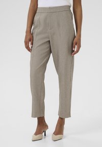 Pantalons ajustés beige en tissu texturé, avec une taille haute, des plis à l'avant et une coupe au niveau des chevilles. Accompagnés de talons beiges.