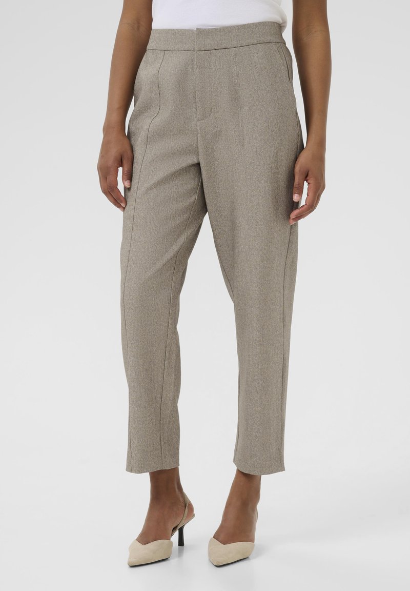 Pantalons ajustés beige en tissu texturé, avec une taille haute, des plis à l'avant et une coupe au niveau des chevilles. Accompagnés de talons beiges.