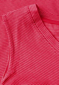 Červený pruhovaný textil, s jemnou strukturou a úzkými bílými pruhy. Design zahrnuje výstřih do V a ploché švy.