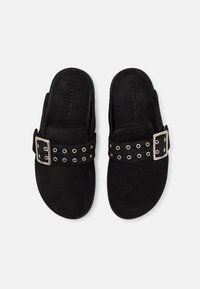 Chaussures à enfiler en suede noir avec une large sangle ornée de détails en métal argenté et d'œillets. Texture lisse et design de bout rond.