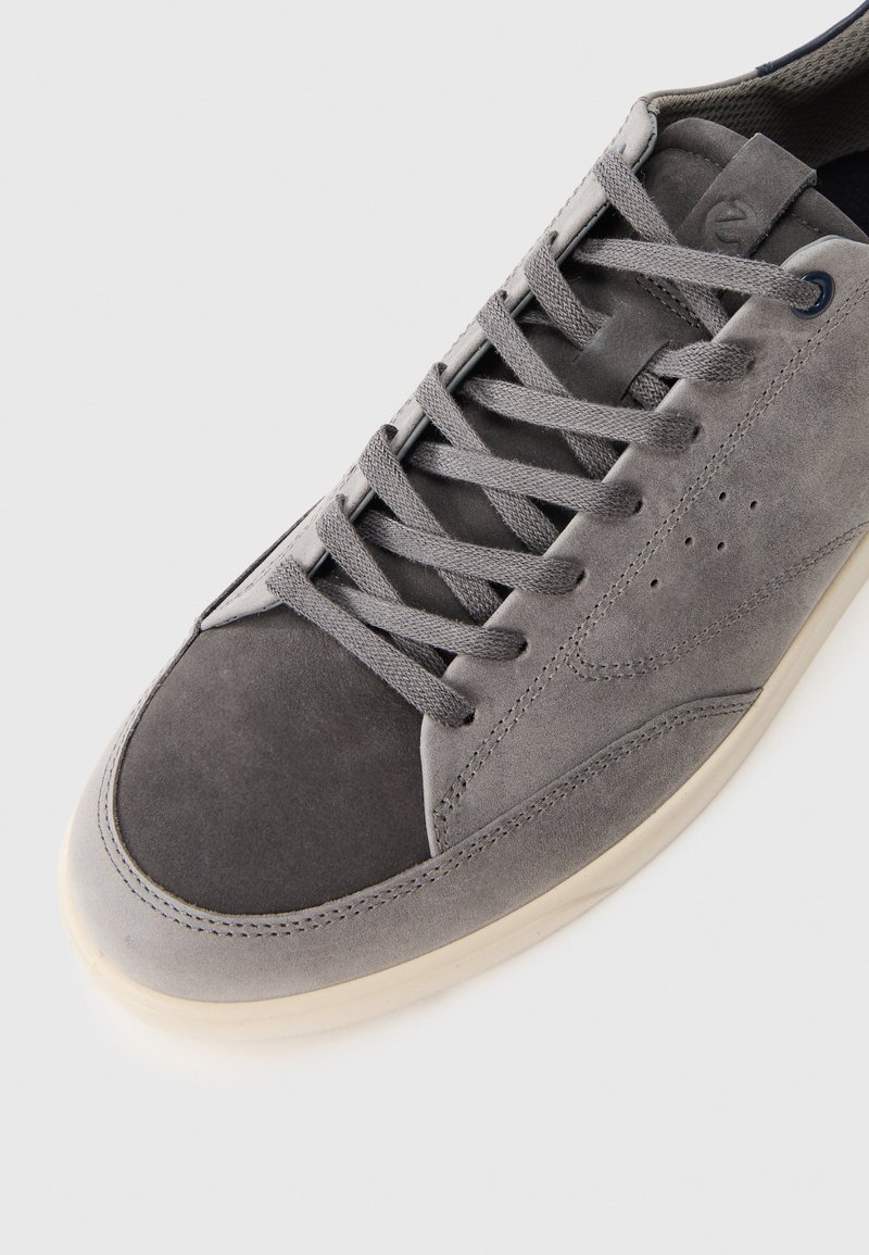 Szare zamszowe sneakersy z gładkim noskiem, teksturowaną cholewką i wyraźnym sznurowaniem. Gumowa podeszwa z subtelnym przeszyciem.