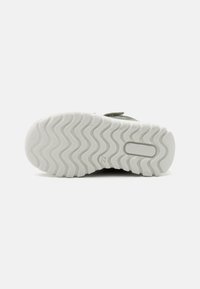 Shoe sole featuring a wavy tread pattern, primarily white rubber, providing traction. Partially visible upper material in green fabric.