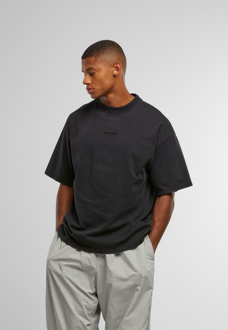 Črna oversize majica iz bombaža z okroglo ovratnikom in kratkimi rokavi; ima subtilno blagovno znamko na sprednji strani. Svetlo sivi hlače.