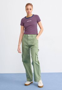 T-shirt a righe a maniche corte in viola e rosso con accenti blu; abbinato a pantaloni cargo verde chiaro con tasche laterali e vestibilità ampia.