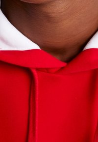 Červená mikina s kapucí z měkké látky s bílou vnitřní podšívkou v oblasti krku, vybavená šňůrkou a jednoduchým, čistým designem.