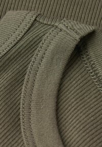 Tejido acanalado de color verde oliva que muestra un borde doblado con un escote liso, presentando finos detalles de costura y una apariencia suave y texturizada.