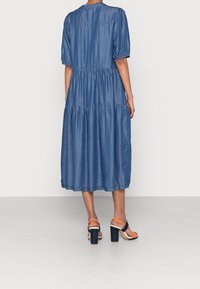 Denimmidiklänning med korta puffärmar, lager på lager volanger och rund halsringning. Kombinerad med klumpiga sandaler med klack och orangea remmar.