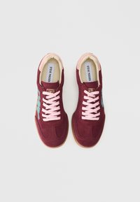 Tumši sarkanas zamšādas sporta apavi ar rozā šņorēm un gumijas zolīti. Aprīkoti ar daudzkrāsainiem akcentiem sānos un mīkstinātu apkakli komfortam.