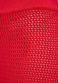 Rood gaasstof met een ruitvormig patroon en een gladde bovenrand. De textuur is lichtgewicht en ademend, ideaal voor sportkleding.
