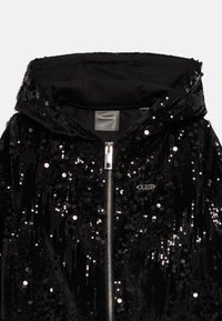 Felpa nera con paillettes, con zip e cerniera argentata, e piccolo logo metallico "GUESS" sul petto.