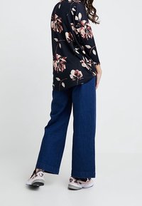 Top negro con flores, decorado con flores rosa claro, combinado con pantalones de denim de pierna ancha. La modelo lleva zapatillas rosa y negro. Colores pastel difusos.