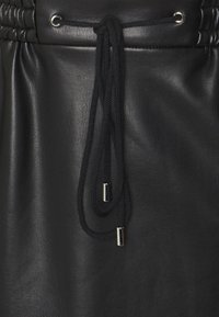 Schwarzes Lederkleidungsstück mit gerafftem Taillenbund und Kordelzug. Der Kordelzug besitzt silberfarbene Metallenden. Glatte Textur, minimales Design.