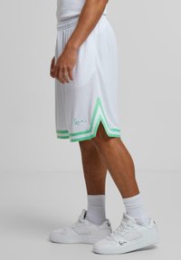 Shorts de sport blancs avec des accents rayés verts et un détail fente sur le côté. Dotés d'une taille élastique avec cordon de serrage et d'un logo brodé.
