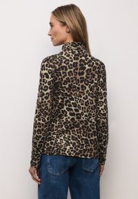Langærmet top med leopardprint og høj hals, med en glat tekstur i nuancer af tan og brun, kombineret med blå denimjeans.