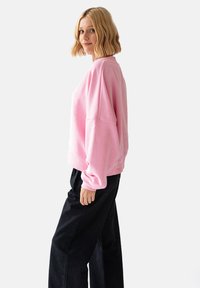 Różowa bluza z opadającymi ramionami i ściągaczami, zestawiona z czarnymi spodniami. Miękka tekstura i luźny krój dla wygody.