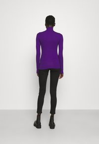 Purple long-sleeve high-neck top, slim fit, paired with black skinny jeans and ankle boots. Smooth texture, no visible patterns or embellishments.