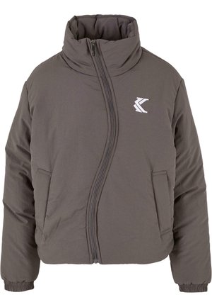 Grå polstret jakke med høj krave, lynlås lukning og sidelommer; har et logo på brystet. Materialet virker glat og let.