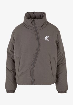 Grå polstret jakke med høj krave, lynlås lukning og sidelommer; har et logo på brystet. Materialet virker glat og let.