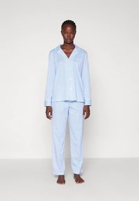 Conjunto de pijama às riscas azuis e brancas, composto por uma camisa com botões, gola e bolso no peito, acompanhada por calças largas a condizer.